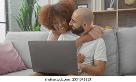 Interracial couple smiling, using laptop together on couch in cozy modern apartment. - Powered by Shutterstock