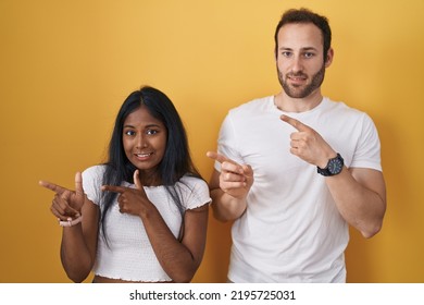 Interracial Couple Standing Over Yellow Background Pointing Aside Worried And Nervous With Both Hands, Concerned And Surprised Expression 