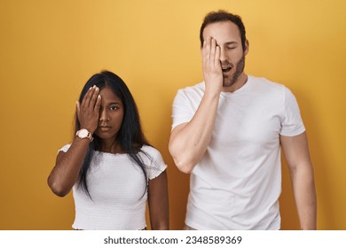 Interracial couple standing over yellow background yawning tired covering half face, eye and mouth with hand. face hurts in pain.  - Powered by Shutterstock