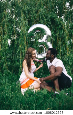 interracial couple walking in the Park in the warm summer day. emotional portrait of students. white girl with long hair and guy African celebrate Valentine's day. balloon in the shape of numbers