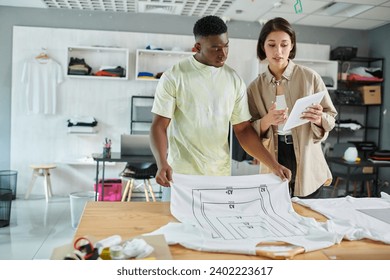 interracial designers looking at digital tablet near t-shirts with format sizes in print studio - Powered by Shutterstock