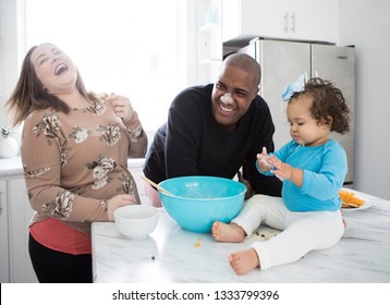 An interracial family having fun in their kitchen with pregnant mother, father, and toddler daughter. - Powered by Shutterstock