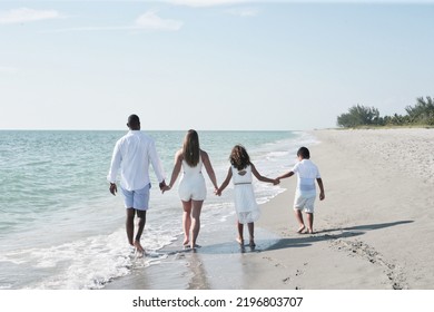 Interracial Family Of People On Vacation Walking Away Together Holding Hands On A Beach On A Sunny Day In Florida In The Water At Water's Edge With Blue Sky