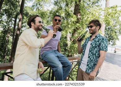 Interracial friends in sunglasses smiling and drinking beer in summer park - Powered by Shutterstock