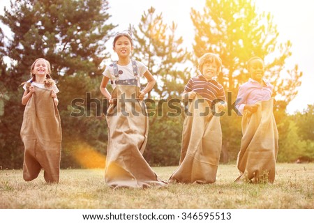 Interracial group of children competing in a sack race at the park