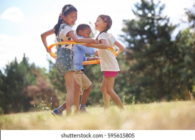 Interracial Group Of Children Playing With Hula Hoop At The Park