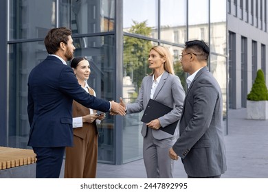 Interracial group of young business people standing on street outside office building in suits, man and woman shaking hands, making deal and getting to know partners and clients. - Powered by Shutterstock