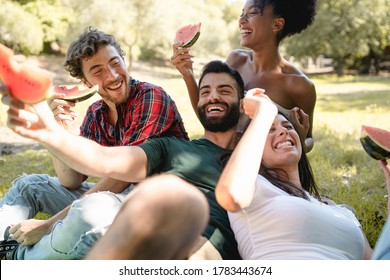 An interracial group of young friends have fun outdoors eating watermelon in the trees of a nature park - Powered by Shutterstock