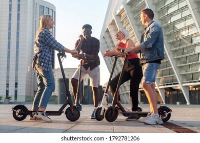 Interracial Group Of Young Friends Ride Electric Scooters In The City And Communicate, Multiracial Young People Use Electric Vehicles And Talk