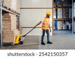 Interracial industrial worker pulling pallet jack full of boxes and goods and preparing shipment at storage.