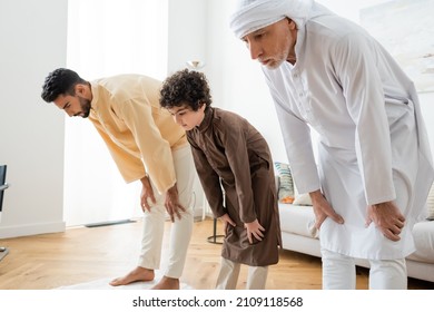 Interracial men and muslim boy bending while praying at home