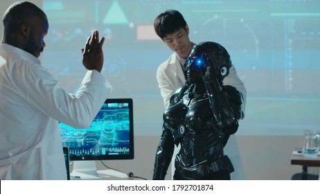 Interracial research team testing the new futuristic automated android in lab. Cybernetic black robot waving hand repeating scientist moves. Artificial intelligence.