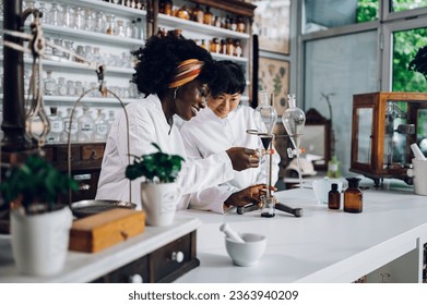 Interracial scientists are using lab equipment and glass funnels in a vintage pharmacy for cure-making. Happy pharmacists are making medicament in a traditional way in a vintage apothecary.