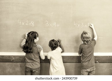 Interracial Students Writing Numbers On Chalkboard At Elementary School.