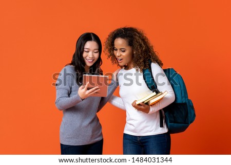 Interracial university students as friends looking at tablet computer isolated on colurful orange background
