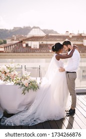 Interracial Wedding Couple. Destination Fine-art Wedding In Florence, Italy. African-American Bride And Caucasian Groom Stand Near The Table For A Wedding Dinner.