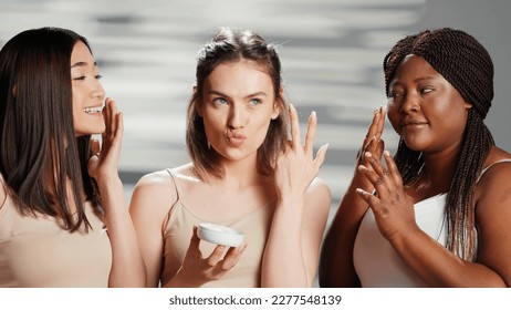 Interracial women applying moisturizing face cream, using skincare cosmetics to prevent wrinkles on camera. Beauty models advertising campaign for dermatology products. Skincare routine. - Powered by Shutterstock