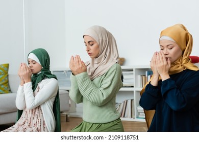 Interracial women in hijabs praying near child at home