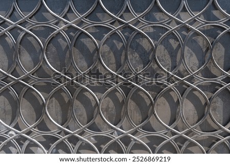 Intersecting circular metal rings create an intricate pattern against a mesh background, casting shadows and creating depth.