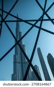 Intersecting steel lines create a bold geometric frame over tall skyscrapers under a bright blue sky.