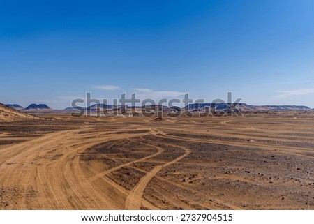 Intersecting tracks across a flat desert floor with rocky plateaus on the horizon near Giza. Visual metaphor for journey, navigation, and human presence.