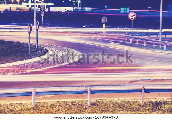 Intersection with car light trails at night,\
focus on guardrail, color toning\
applied.