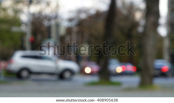 Intersection\
with cars taken in a blurred un-focused shot. Pedestrian walkway\
and trees in the front. Car lights\
visible.