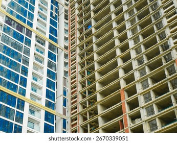 Intersection corner between beige-framed glass tower stand beside exposed concrete floors of unfinished building still skeletal, illustrating development progress and city expansion in Danang. Vietnam
