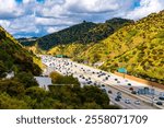 “California Interstate 405” or ‘San Diego Freeway’ is a busy multi-lane highway in the metropolis of Los Angeles (USA). Numerous cars drive on a section of the road in the sunny hills of the city.