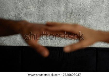 Intertwined hands of woman and man of african ethnicity unfocused outstretched towards each other, selective focus on gray textured background. Love, affection and passionate relationships