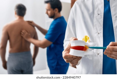 Intervertebral hernia treatment. Chiropractor with anatomical lumbar disc herniation model while consultation of man with back pain - Shutterstock ID 2284940797