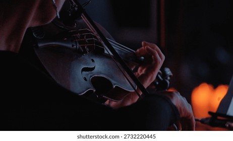 Intimate close-up of a violinist performing. Dramatic low-key lighting with warm, soft highlights illuminates the instrument hands. The moody, dark atmosphere suggests passion, focus, elegance