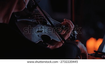 Intimate close-up of a violinist performing. Dramatic low-key lighting with warm, soft highlights illuminates the instrument hands. The moody, dark atmosphere suggests passion, focus, elegance