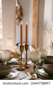 Intimate dining table scene featuring peach taper candles in brass holders beside green textured glassware, styled for a wedding reception or cozy dinner party