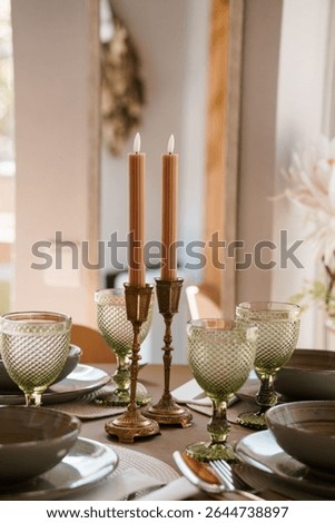 Intimate dining table scene featuring peach taper candles in brass holders beside green textured glassware, styled for a wedding reception or cozy dinner party