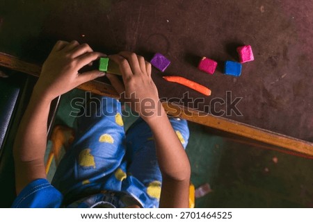 An intimate, high-angle, overhead shot captures a child's hands fully absorbed in creative play on a dark, rustic wooden table. The hand carefully manipulating a piece of vibrant green modeling clay.