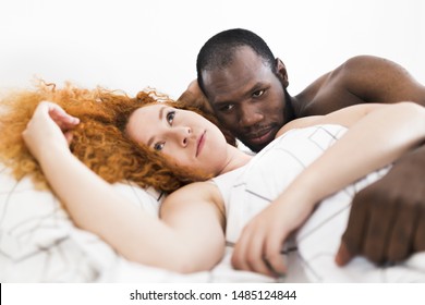 Intimate moment of interracial couple in bed in a photo studio with white background