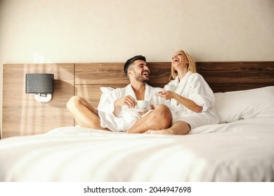 Intimate moments in bed with morning coffee. Romantic shot of two lovers drinking coffee in warm robes. A man and a woman look happy and fulfilled as they talk. Full of love, sharing beautiful moments - Shutterstock ID 2044947698