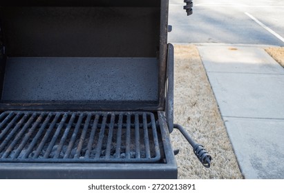 An intimate perspective looking into the interior of a heavy-duty black metal charcoal grill. The image features the internal rusted grate and the dark textured walls of the firebox, representing themes of community athletics, social dining, and the maintenance of public park facilities. The lighting is natural and highlights the industrial patina of the hardware and the fine char residue on the metal. This image conveys themes of shared urban services and the unpolished side of metropolitan lifestyle. It is an ideal visual for technical blogs, maintenance guides, and architectural studies of outdoor furniture. The focused composition captures the functional and sturdy energy of the shared equipment, providing an authentic look at the recreational amenities that support active community life in areas like Philadelphia. The raw and unpolished aesthetic adds an atmospheric layer to the mundane city scene, illustrating the practical components of city-center land care and property oversight.
