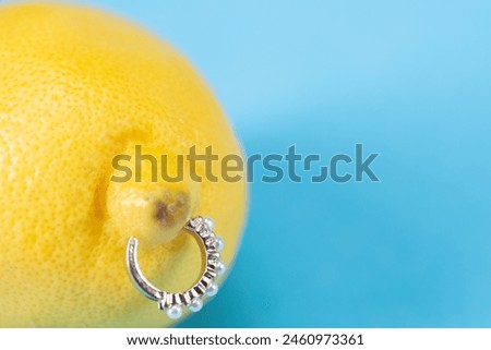 Intimate piercing. Minimal piercing concept. Lemon with piercing on blue background.