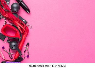 Intimate sex games. BDSM Tools dildo vibrator, gag, nipple clamps, handcuffs, whip and other on red pink background. Free space for your text
