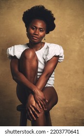 Intimate Studio Portrait Of African Black Woman Sit On Stool Against Yellow Grunge Background. 