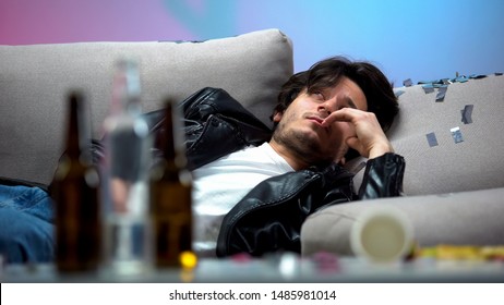 Intoxicated Young Man Waking Up On Messy Couch After Party, Looking Around