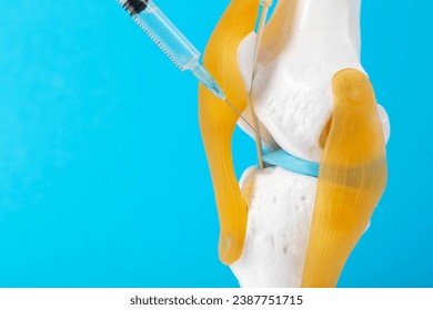 Intra-articular injection of anti-inflammatory medication into a mock-up knee joint on a blue background. The concept of drug blockade to relieve pain and inflammation. Copy space for text