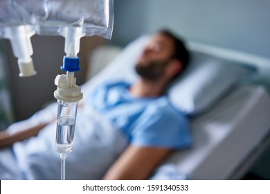 Intravenous drip treatment being used to treat a sick man lying on a bed in a hospital 