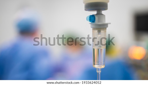Intravenous fluid\
infusion during advance surgery inside operating room.Surgeon doing\
emergency surgery.Saline pump set drip to blood loss patient with\
blur background.Medical\
concept.