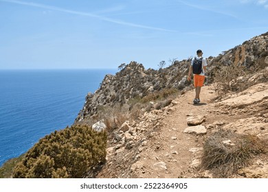 Intrepid Male Traveler Conquering Challenging Coastal Hiking Trail Amidst Dramatic Rocky Landscape and Turquoise Waters - Powered by Shutterstock