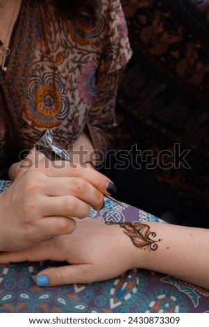 Intricate henna feather tattoo on a woman's wrist, paired with a patterned blouse and bold nail polish
