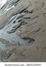 Intricate river-like patterns and textures created by receding tide water on a dark volcanic sand beach
