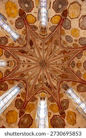 Intricate star patterned painted ceiling vault with colorful stained glass window accents in a historic building